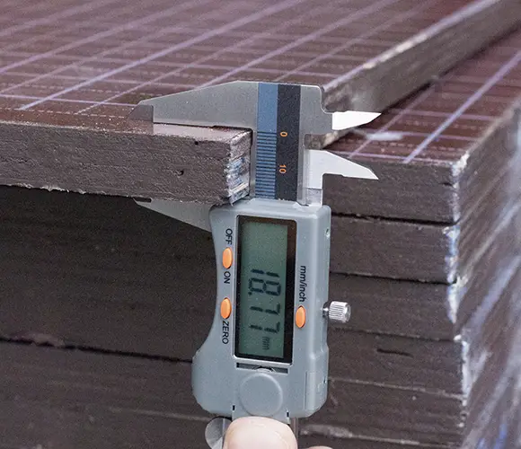 Paquímetro medindo chapa de compensado plastificado 18mm da Infinity Compensados, com filme fenólico para formas de concreto na construção civil.
