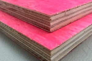 Chapas de madeirite resinado cola branca (compensado rosa) empilhadas, com foco nas camadas e na borda do painel.